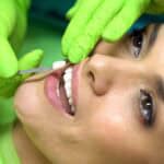 Dentist holding a veneer up to a patient’s front tooth for placement.