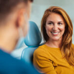 Smiling red haired woman listening to her dentist while sitting in his office
