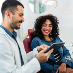 Mid adult dentist man using digital tablet and talking to young patient woman at dentist's office