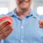 Adult holding braces and a clear aligner to compare Invisalign vs. braces